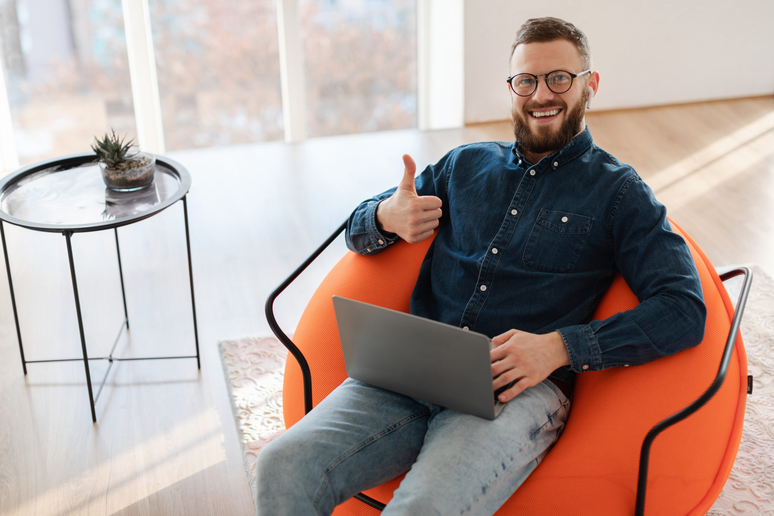 Smiling Male Freelancer Using Laptop Computer Gesturing Thumbs Up Approving Website For Distance Freelance Work Looking At Camera Sitting In Chair At Home, Wearing Eyeglasses. I Like Remote Job